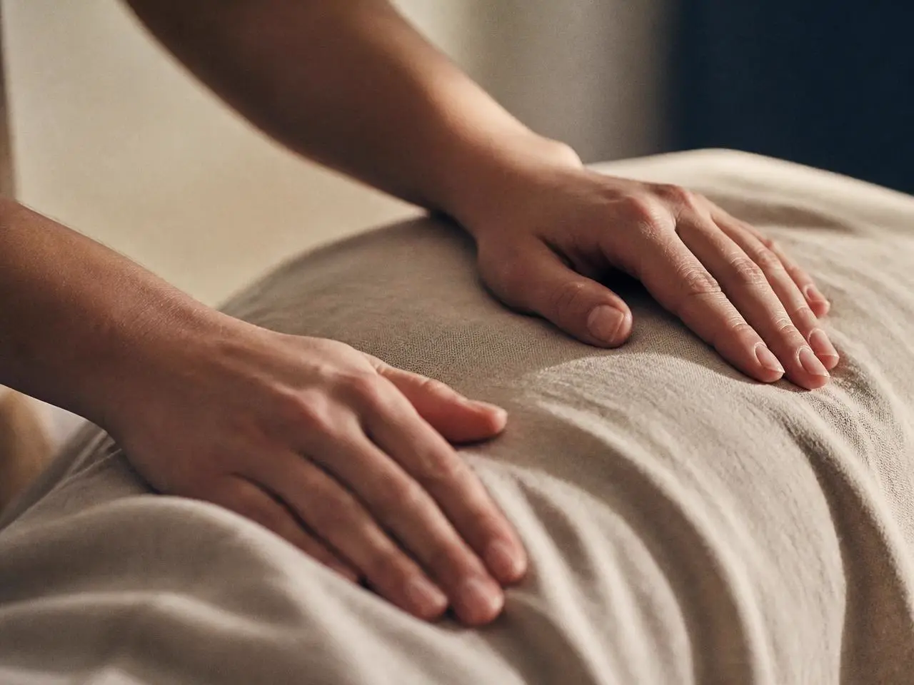 Twee handen rusten zacht op een linnen doek tijdens een massage